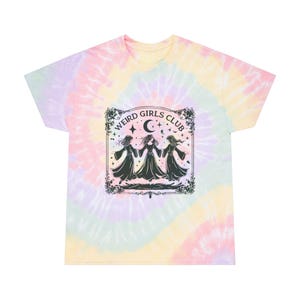 May include: A tie-dye t-shirt with a black and white graphic of three figures in a circle with the text "Weird Girls Club" in a decorative frame.