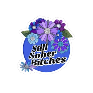 May include: A sticker featuring a blue circle with the text "Still Sober Bitches" in black. The circle is surrounded by various purple and blue flowers with green leaves. The flowers have white and silver accents.