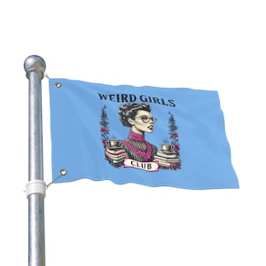 May include: A light blue flag with the words "WEIRD GIRLS CLUB" and an illustration of a woman wearing glasses, holding a cup of coffee, and standing in front of a stack of books. The flag is attached to a silver pole.