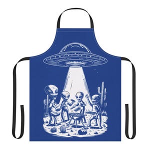 Puede incluir: Delantal azul con una ilustración blanca de extraterrestres haciendo una barbacoa bajo un OVNI. El diseño incluye un OVNI, extraterrestres, una parrilla y plantas del desierto. El delantal tiene correas negras y un lazo para el cuello.