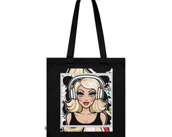 May include: Black tote bag featuring a cartoon illustration of a blonde woman wearing headphones. The woman has long, wavy hair, red lipstick, and a black top. The background has colorful paint splatters.