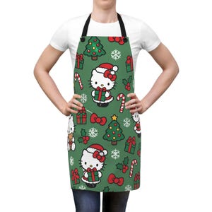 May include: A green apron featuring a repeating Christmas-themed pattern of Hello Kitty wearing a Santa hat, decorated pine trees, red gift boxes with green ribbons, candy canes, white snowflakes, holly berries, and red bows on a dark green background.
