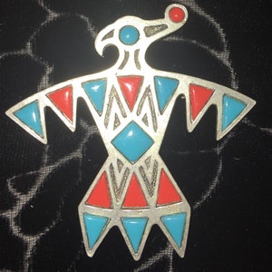 May include: A silver-toned pendant in the shape of a stylised bird with turquoise and red enamel accents. The bird has a long beak and spread wings.