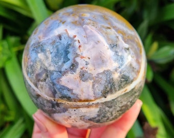 Puede incluir: Una esfera de ágata pulida con una variedad de colores, incluyendo blanco, marrón, gris y verde. La esfera es lisa y tiene un aspecto natural y orgánico.