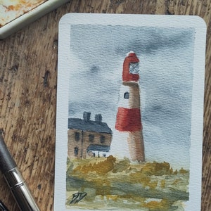 May include: Watercolour painting of a red and white lighthouse with a grey cloudy sky in the background. A small brown building is visible in the foreground.