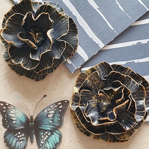 Peut inclure: Deux ornements floraux foncés avec des accents dorés sont présentés. Un autocollant de papillon bleu et blanc est également visible. L'arrière-plan comprend un motif à rayures bleues et blanches.