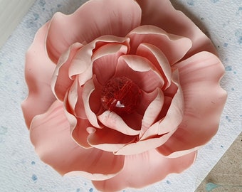 May include: A delicate pink flower with a red glass bead in the center. The flower is made of polymer clay and has a realistic appearance.