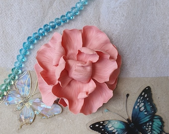 May include: A pink fabric flower with a ruffled texture, a blue iridescent butterfly, and a light blue crystal beaded necklace.