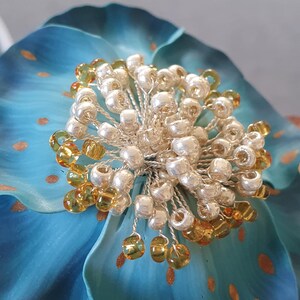 Pode incluir: Uma flor azul com um centro feito de contas prateadas e douradas.