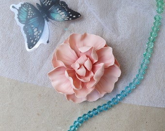 May include: A pale pink fabric flower with a delicate, layered design. The flower is surrounded by a strand of turquoise blue beads.
