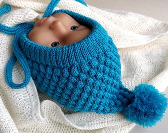 May include: A turquoise knitted baby hat with a pom-pom on top. The hat has a textured design and is tied with a matching turquoise ribbon.