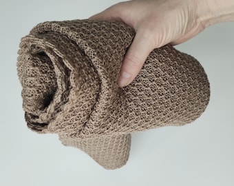Pode incluir: Um cobertor de malha marrom enrolado em uma mão. O cobertor tem uma textura de waffle.