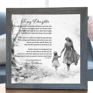 Puede incluir: Un marco de madera gris que contiene una ilustración en blanco y negro de una madre y su hija caminando juntas. El texto "To my Daughter" está en la parte superior, con un poema debajo. El marco está sobre una mesa de madera.