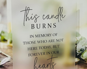 May include: A frosted acrylic sign with black text that reads "This candle burns in memory of those who are not here today, but forever in our hearts". A small heart symbol is below the text.