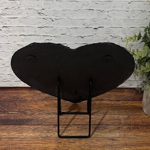 May include: Black heart-shaped slate plaque with a black metal stand. The plaque has two small metal circles on the back.