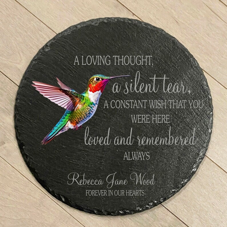 May include: Black slate round memorial plaque with a colorful hummingbird illustration and the text "A loving thought, a silent tear, A constant wish that you were here loved and remembered always Rebecca Jane Wood Forever in our hearts".