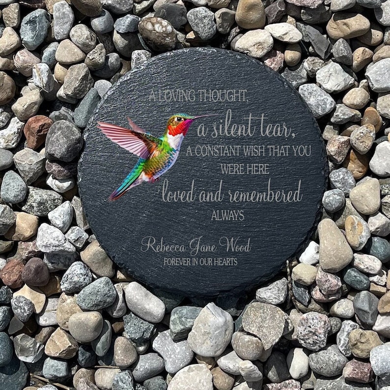 May include: A black slate stone memorial with a hummingbird image and the text "A loving thought, a silent tear, A constant wish that you were here loved and remembered always Rebecca Jane Wood Forever in our hearts".
