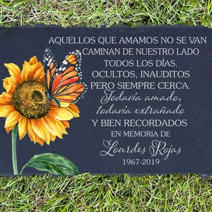 May include: A black slate memorial stone with a sunflower and butterfly design. The stone has a white inscription that reads "Aquellos que amamos no se van Caminan de nuestro lado Todos los días. Ocultos, inaudito Pero siempre cerca. Todavía amado, todavía extrañado Y bien recordados En memoria de Lourdes Rojas 1967-2019"