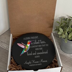 May include: A black slate round with a colorful hummingbird image and the text "A loving thought, a silent tear, A constant wish that you were here loved and remembered always Angela Karen Marcus Forever in our hearts".