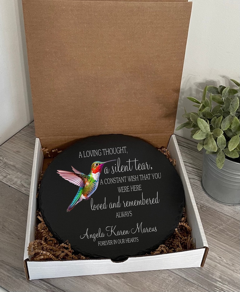 May include: A black slate round with a colorful hummingbird image and the text "A loving thought, a silent tear, A constant wish that you were here loved and remembered always Angela Karen Marcus Forever in our hearts".