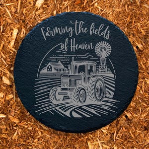 May include: Black slate round sign with the text "Farming the fields of Heaven" and a black and white illustration of a tractor in a field.