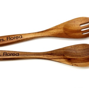 May include: A wooden salad fork and a wooden salad spoon with a smooth, polished finish. The handle of the fork is engraved with the text Mrs. Florea, and the handle of the spoon is engraved with the text Mr. Florea in a dark, sans-serif font.