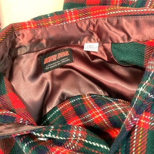 Puede incluir: Primer plano de una chaqueta a cuadros con patrones rojos, verdes y blancos. La chaqueta tiene un forro de sat&eacute;n marr&oacute;n y una etiqueta que dice "NORTH TRAIL A PERFECTION FABRIC FOR WARMTH AND STRENGTHEN."
