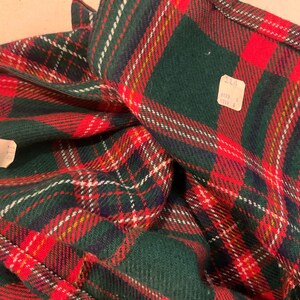 Puede incluir: Primer plano de una tela a cuadros doblada en rojo, verde, blanco y amarillo. El patr&oacute;n es un dise&ntilde;o tart&aacute;n cl&aacute;sico. Se ven dos etiquetas de precio. La tela parece ser un material pesado, posiblemente lana o una mezcla de lana.