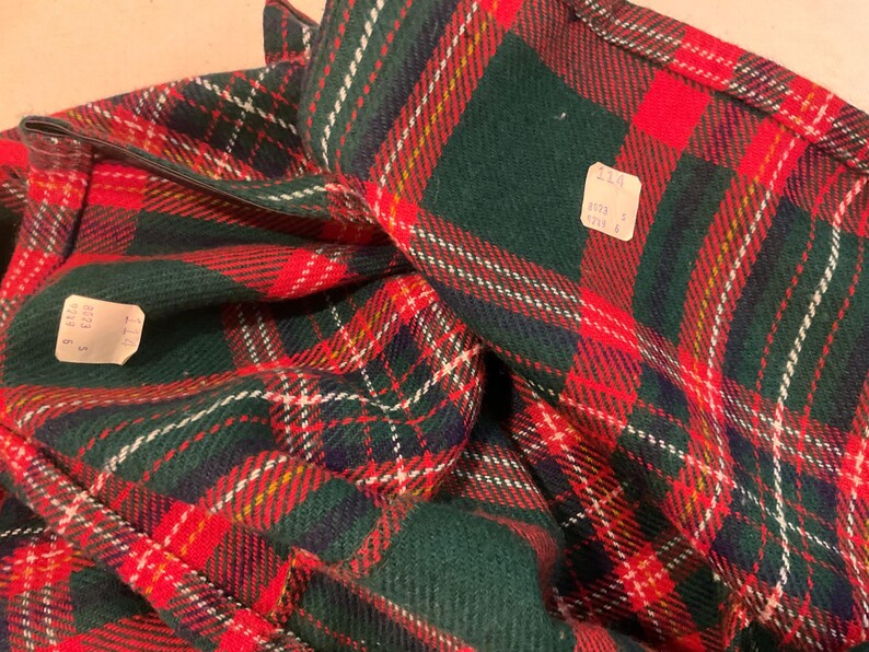 Puede incluir: Primer plano de una tela a cuadros doblada en rojo, verde, blanco y amarillo. El patr&oacute;n es un dise&ntilde;o tart&aacute;n cl&aacute;sico. Se ven dos etiquetas de precio. La tela parece ser un material pesado, posiblemente lana o una mezcla de lana.