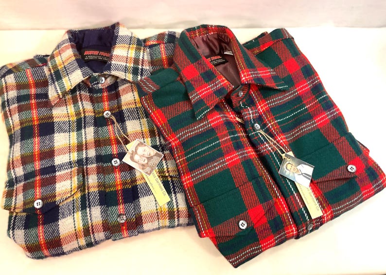 Puede incluir: Dos camisas de franela a cuadros. Una camisa presenta un patr&oacute;n de amarillo, naranja, verde y azul marino. La otra camisa tiene un patr&oacute;n de cuadros rojo y verde. Ambas camisas tienen cierres de botones y etiquetas colgantes.