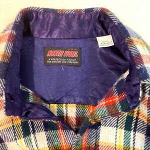 Puede incluir: Primer plano de una camisa de cuadros vintage con forro y cuello de sat&eacute;n morado. La camisa presenta un colorido estampado de cuadros en rojo, verde, amarillo y blanco. La etiqueta dice "NORTH TRAIL" y "100% Acrylic".