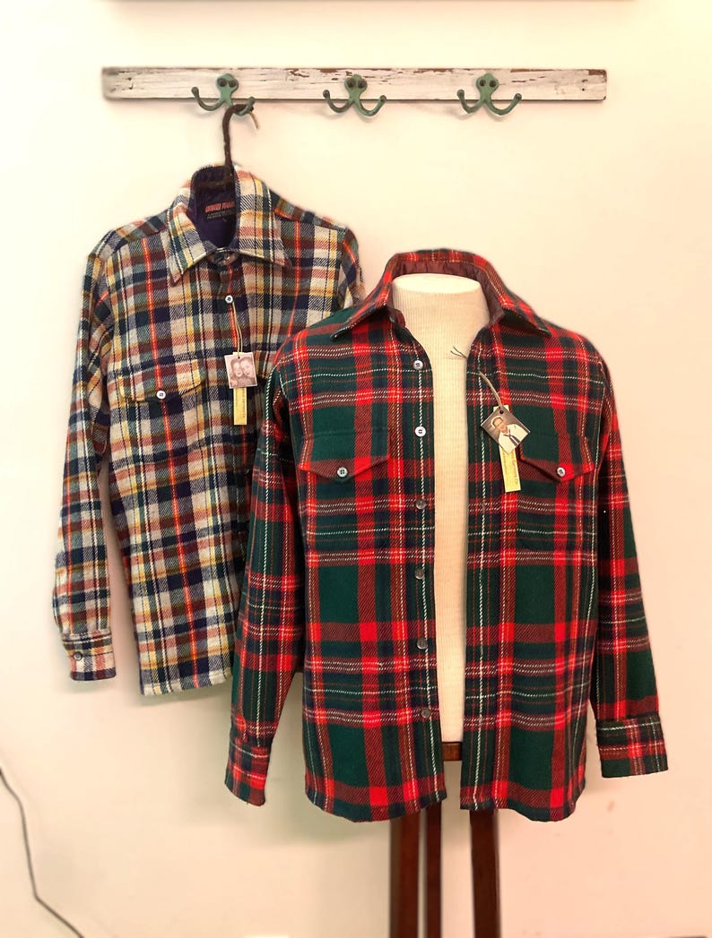 Puede incluir: Dos camisas de franela a cuadros, una colgando y otra en un maniqu&iacute;. La camisa colgante tiene un patr&oacute;n azul, rojo, amarillo y blanco. La camisa del maniqu&iacute; es roja y verde. Ambas camisas tienen cuello y cierre de botones.