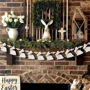 May include: A handmade wooden sign with the text "Welcome" in a playful font. The sign is painted white with a distressed finish, and features a decorative floral design in shades of pink and green. It measures approximately 12 inches wide.