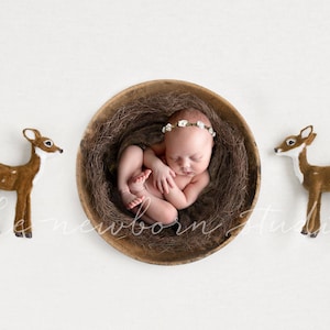 May include: A newborn baby wearing a floral headband is nestled in a wooden bowl filled with brown nesting material. Two brown deer figurines with white spots flank the bowl. The image has a soft, neutral color palette.