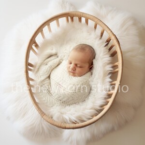May include: A sleeping newborn baby wrapped in a cream blanket, inside a wicker basket. The basket sits on a fluffy white faux fur rug. The text "the newborn studio" is visible.