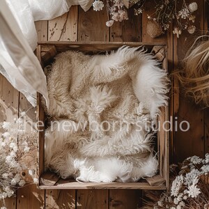May include: A wooden crate with a white fluffy blanket inside. The crate is sitting on a wooden floor with dried flowers and greenery around it.