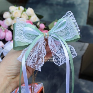Peut inclure: Un nœud en dentelle blanche avec un ruban de satin vert et des rubans de satin blanc. Le nœud est noué avec une ficelle en ficelle brune.
