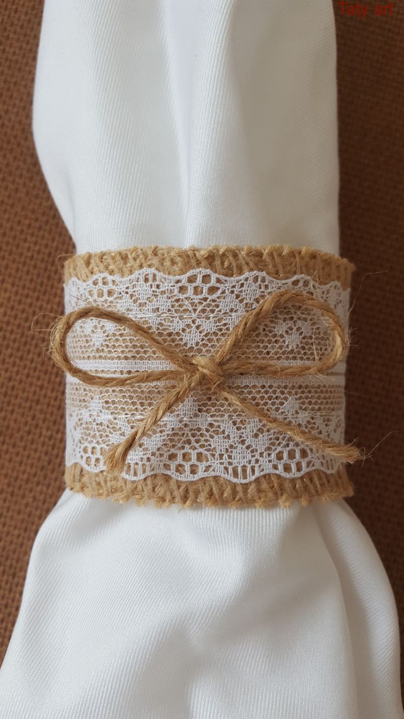 May include: A burlap napkin ring with a white lace trim and a brown twine bow.