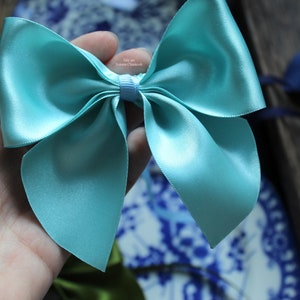Peut inclure: Gros plan sur un nœud en satin de couleur turquoise clair. Le nœud est tenu dans une main, avec d'autres nœuds de différentes couleurs en arrière-plan. Le nœud est noué avec un petit ruban au centre.