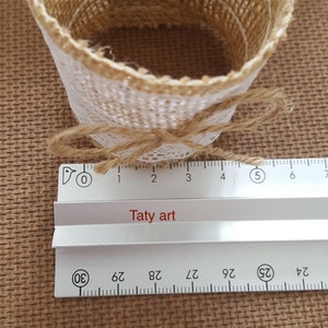 May include: A brown burlap napkin ring with a white lace trim and a brown twine bow. The ring is 5 inches in diameter.