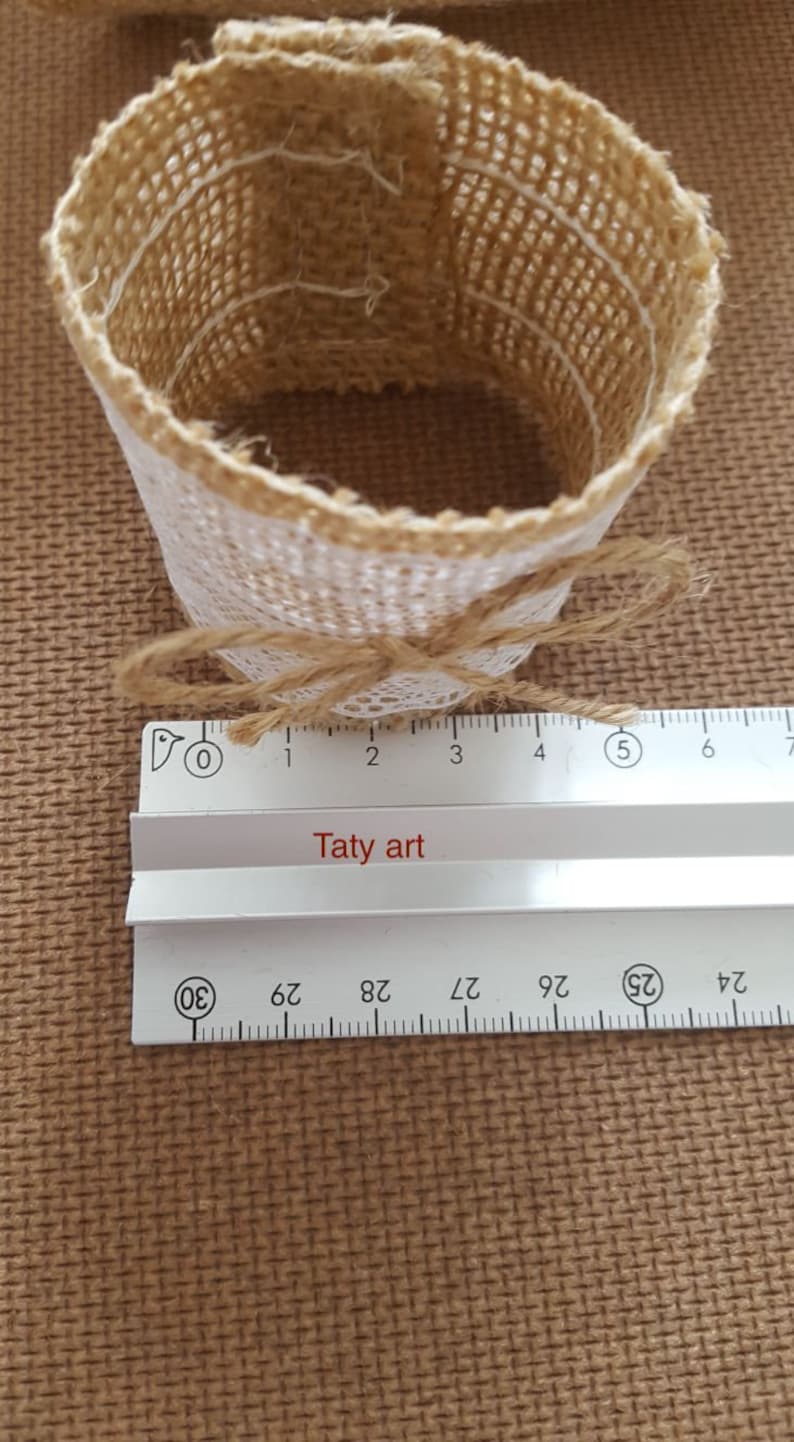 May include: A brown burlap napkin ring with a white lace trim and a brown twine bow. The ring is 5 inches in diameter.