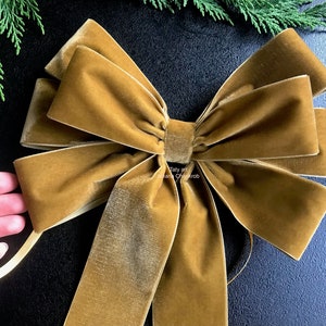 May include: A large, golden-brown velvet bow. The bow has multiple loops and tails, with a soft, textured appearance. The bow is likely for decoration, possibly for a gift or holiday decor.