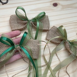 Peut inclure: Trois nœuds en toile de jute avec des rubans verts et dorés. Les nœuds sont noués avec un simple nœud et les rubans sont longs et flottants.