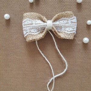 Peut inclure: Un n&oelig;ud en toile de jute marron avec une garniture en dentelle blanche et une ficelle en ficelle blanche. Le n&oelig;ud est sur un fond textur&eacute; marron avec des perles de perles blanches &eacute;parpill&eacute;es autour. Le texte "Taty art" est dans le coin sup&eacute;rieur droit de l'image.