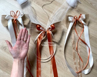 Può includere: Tre fiocchi di juta con nastro bianco e arancione, legati con un fiocco di tulle bianco. I fiocchi sono disposti su una superficie di legno. Il testo "Idea Tatytart Tetiana Chankrob" è visibile nell'immagine.
