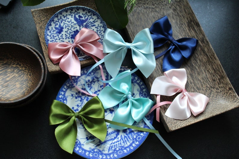 Puede incluir: Surtido de lazos de sat&eacute;n en varios colores, incluyendo rosa, azul y verde. Los lazos est&aacute;n dispuestos sobre platos decorativos azules y blancos y una bandeja de madera, ideal para manualidades o envolver regalos.