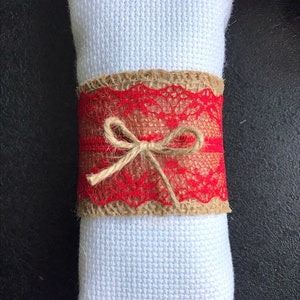 May include: A red lace and burlap napkin ring with a brown twine bow.