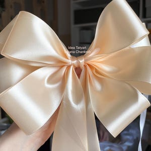 Peut inclure: Un grand nœud en satin de couleur pêche. Le nœud est noué au centre avec plusieurs boucles et des rubans. Le satin a un léger éclat, reflétant la lumière. Le nœud est probablement utilisé pour la décoration ou l'emballage de cadeaux.