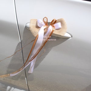 Puede incluir: Una puerta de coche blanca con un lazo de arpillera decorado con cinta blanca y dorada. El lazo está atado al tirador de la puerta. El texto "Taty art Tatiana Chankrob" está impreso en la puerta del coche.