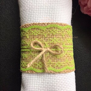May include: A white napkin with a green and brown burlap napkin ring tied with twine. The ring has a lace design.